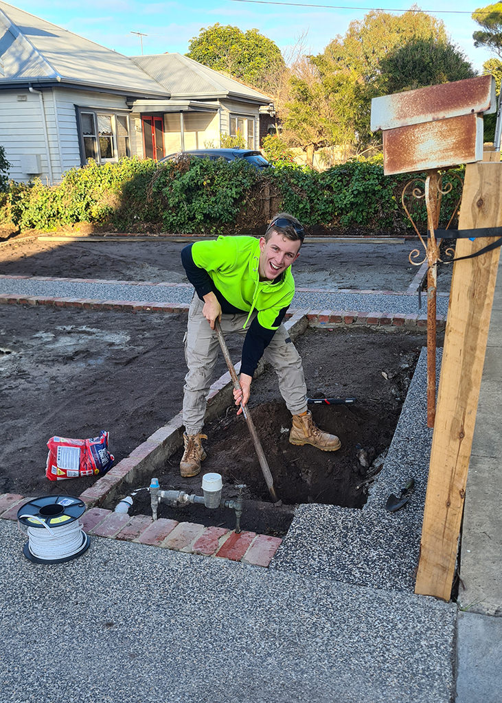 A young and happy Electrician apprentice digging a hole.