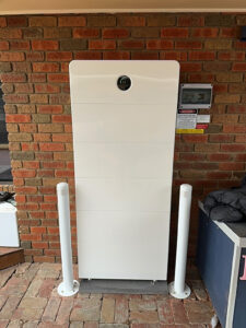 Large Sigenergy SigenStor home battery stack installed against a red brick wall with bollards.