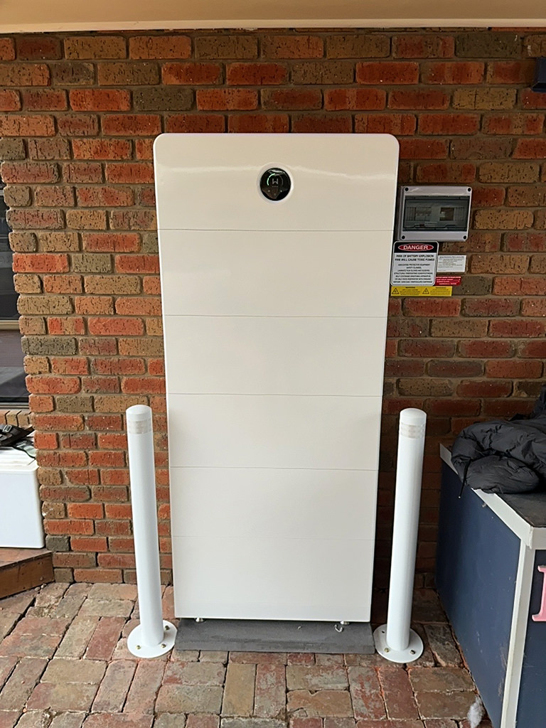 Large Sigenergy SigenStor home battery stack installed against a red brick wall with bollards.