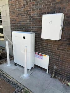 Sigenergy SigenStor battery and inverter system installed on an external brick wall with safety signage.